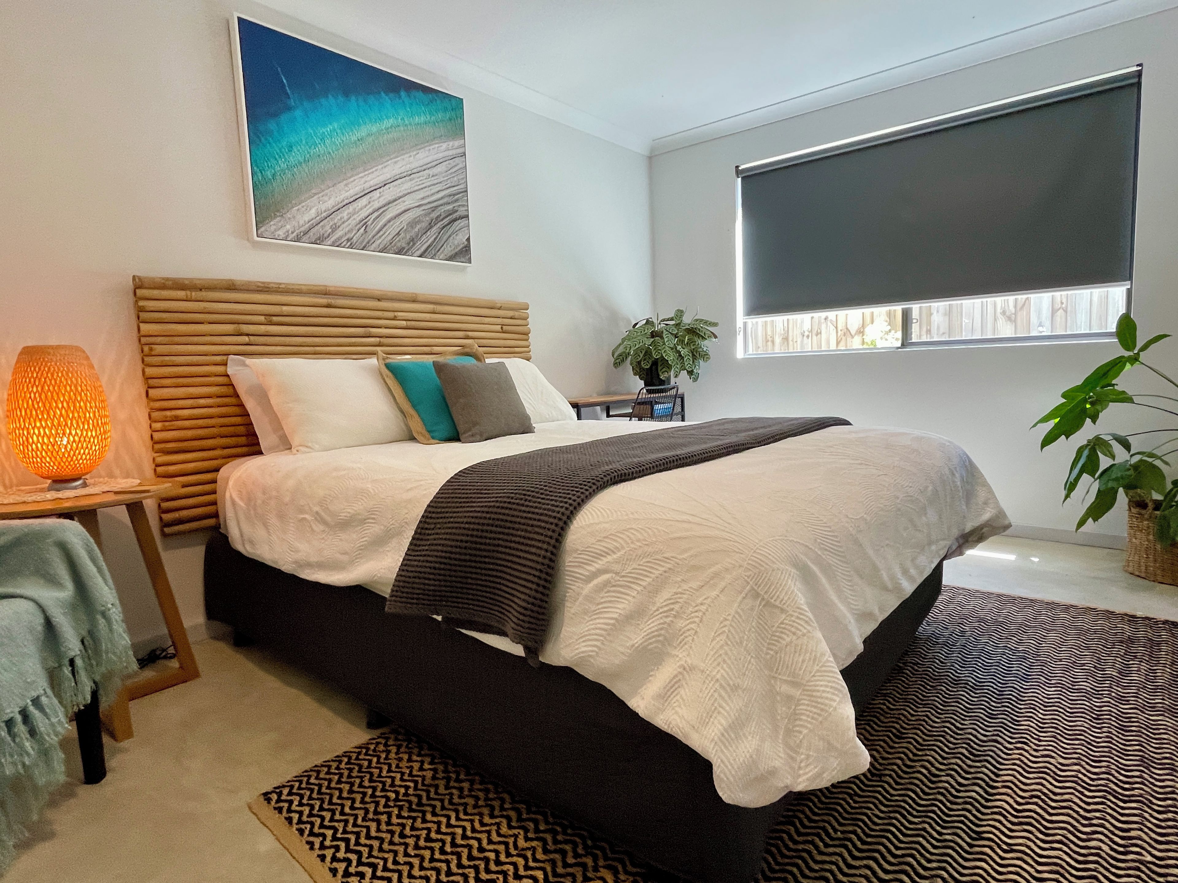 A bedroom with a bed, bedside table, lamp, and a window with blinds.