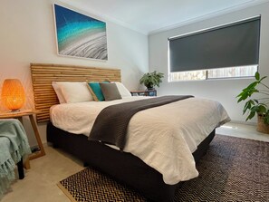 A bedroom with a bed, bedside table, lamp, and a window with blinds.