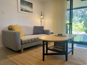 Ein Wohnzimmer mit einer Couch, einem runden Holztisch, einer Lampe und einem Bücherregal.