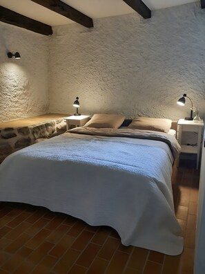 Ein Schlafzimmer mit Steinwand, einem Bett mit weißer Bettdecke, zwei Nachttischlampen und einem kleinen Nachttisch mit einer Vase.