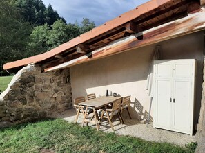 Eine Steinsäule mit einem Holztisch und Stühlen, einem weißen Schrank und einem geneigten Dach.