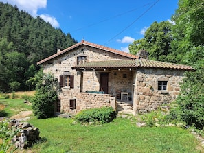 Ein Steinhhaus mit Ziegeldach, umgeben von Grün und mit Blick auf die Berge.