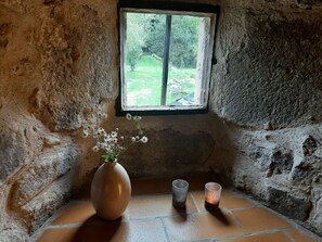 A rustic room with a stone wall, a small window, a vase with flowers, and two candle holders. - Holiday Home 'Du Moulin' with Mountain View, Private Terrace and Wi-Fi (Pailharès)