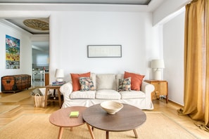 A living room with a white sofa, two side tables, a bowl on one table, and a painting on the wall. - SMG Boutique Apartment (Athina)