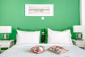 A bed with white linens, two green pillows, and two white pillows with floral patterns. There is a framed picture on the wall above the bed. - SMG Boutique Apartment (Athina)