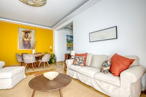 A living room with a white sofa, a round coffee table, and a yellow accent wall. - SMG Boutique Apartment (Athina)