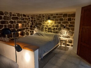 Ein Schlafzimmer mit Steinwand, einem Bett, einem Schreibtisch mit Lampe und einem kleinen Tisch.