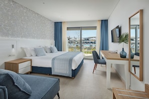 Ett modernt hotellrum med en säng, ett skrivbord, en stol, en TV och utsikt över en pool och byggnader.