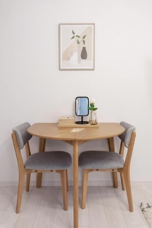 A round wooden dining table with two grey upholstered chairs, a framed artwork above, and a small vase with a plant on the table. - SunLight Kishinosato (Osaka, Nishinari-ku)