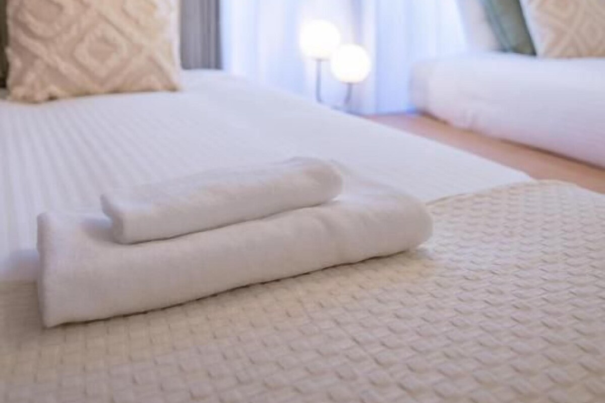 A hotel room with a bed, a bedside table, and a window with curtains.