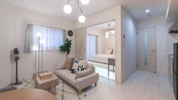 A modern living room with a sofa, coffee table, and a dining area. There is a large mirror, a plant, and a clock on the wall.