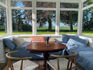 Ein Zimmer mit einem großen Fenster, einem runden Holztisch und einem blauen Sofa mit Kissen.