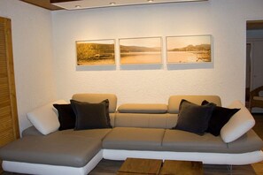 Una sala de estar moderna con un sofá seccional, una mesa de centro y tres fotografías enmarcadas de paisajes en la pared.