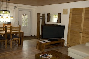 A living room with a wooden TV stand, a sofa, a dining table with chairs, and a wooden wardrobe. - Cuckoo House Premium (Titisee-Neustadt)