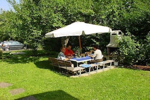 An outdoor dining area with a table and chairs under a white umbrella, surrounded by greenery. - Rolf Bauer on the ground floor (Konstanz)
