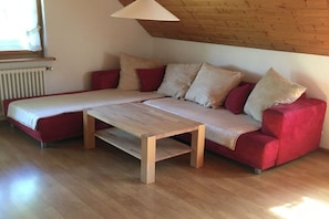 A red sofa with a wooden table in a room with wooden flooring and a sloped ceiling. - Holiday apartment with 1 bedroom (Seelbach)