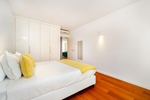 A bedroom with a bed, white walls, a wooden floor, and a closet. - Bright & Modern T1 near Tagus River (Algés)