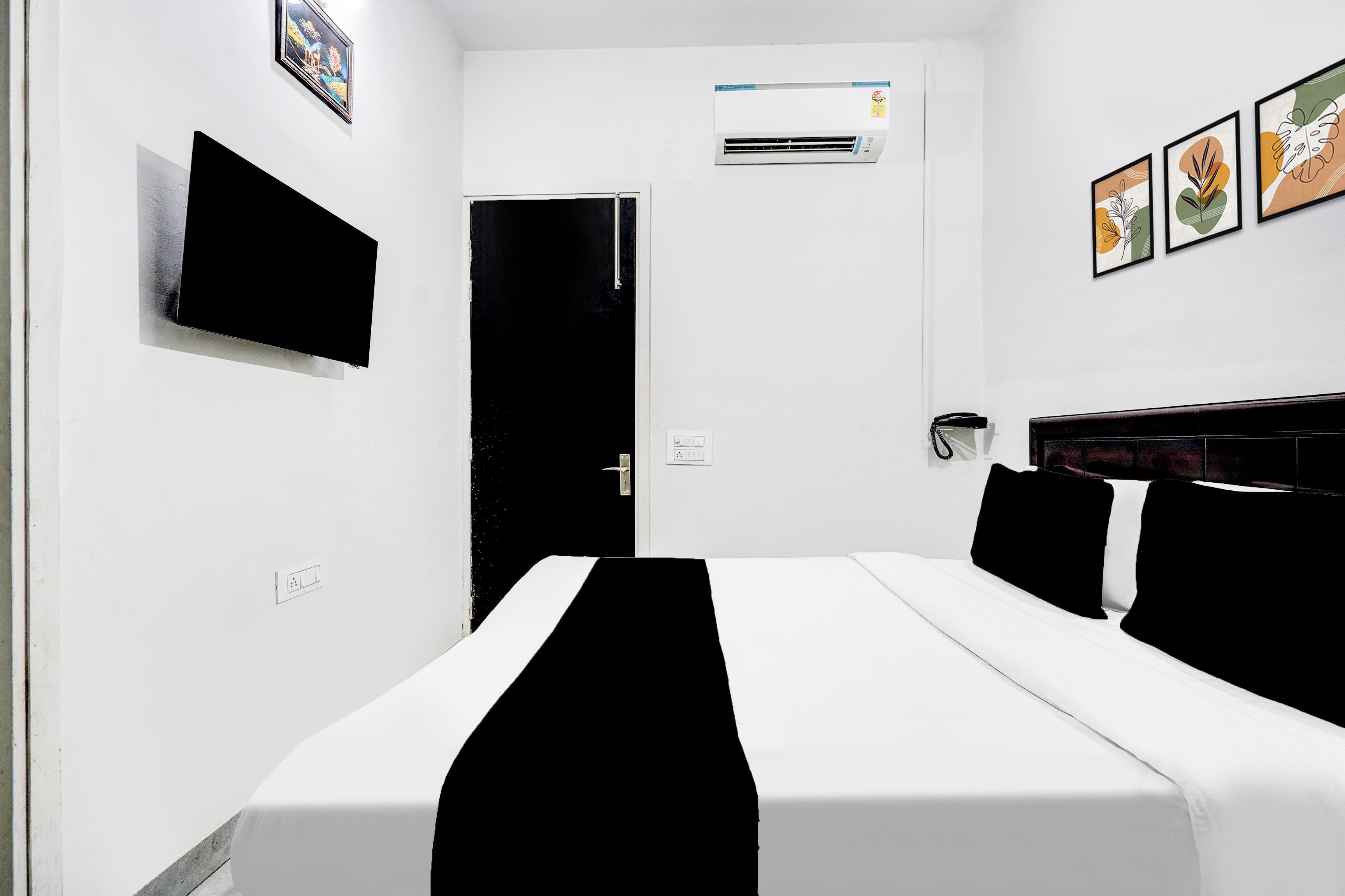 A hotel room with a bed, a flat-screen TV, an air conditioning unit, and a door.