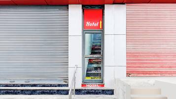 Entrada de un hotel con un letrero rojo, una puerta con persiana cerrada y una escalera que sube a la entrada.