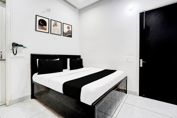 A modern bedroom with a black and white bed, a door, and three framed artworks on the wall.