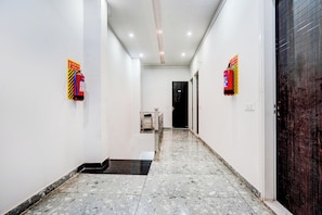 A corridor with white walls, a tiled floor, and two fire extinguishers mounted on the walls.