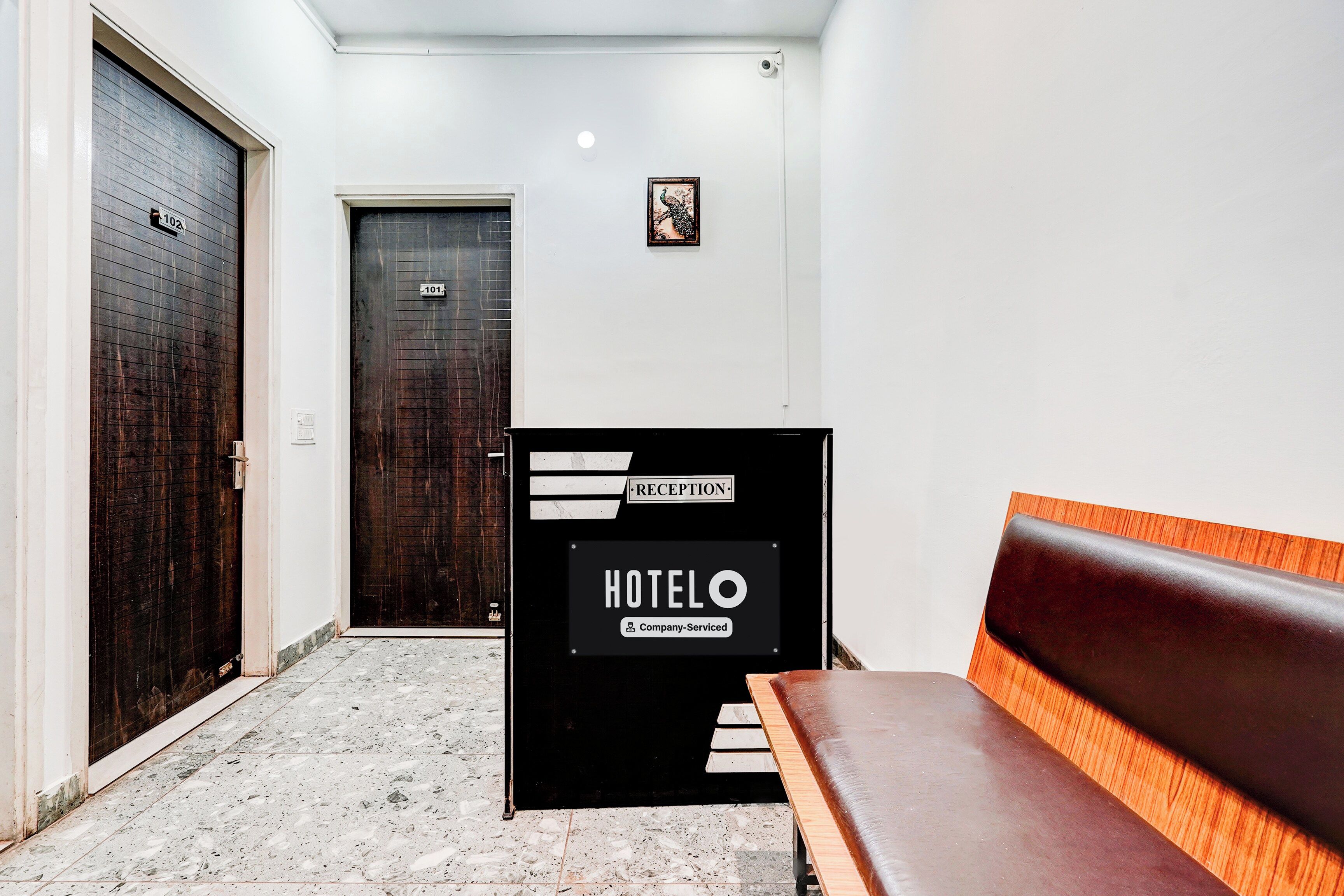 Zona de recepción de un hotel con mostrador, un banco y dos puertas.