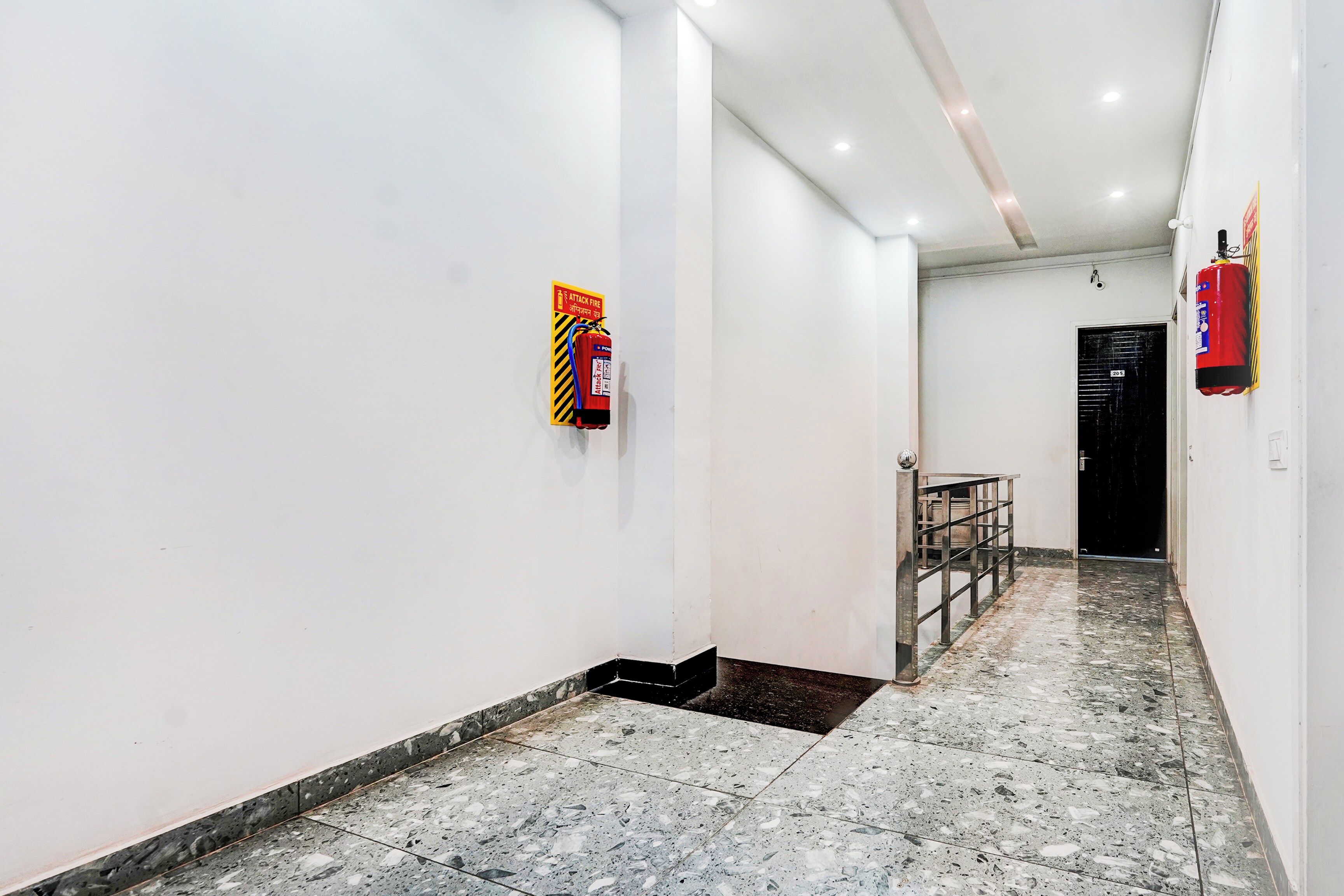 Un pasillo con paredes blancas, piso de baldosas y un extintor de incendios colgado en la pared.