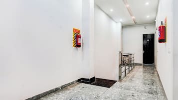 Un pasillo con paredes blancas, piso de baldosas y un extintor de incendios colgado en la pared.