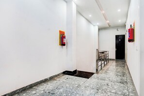 A corridor with white walls, a tiled floor, and a fire extinguisher mounted on the wall.