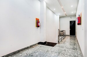 Un pasillo con paredes blancas, piso de baldosas y un extintor de incendios colgado en la pared.