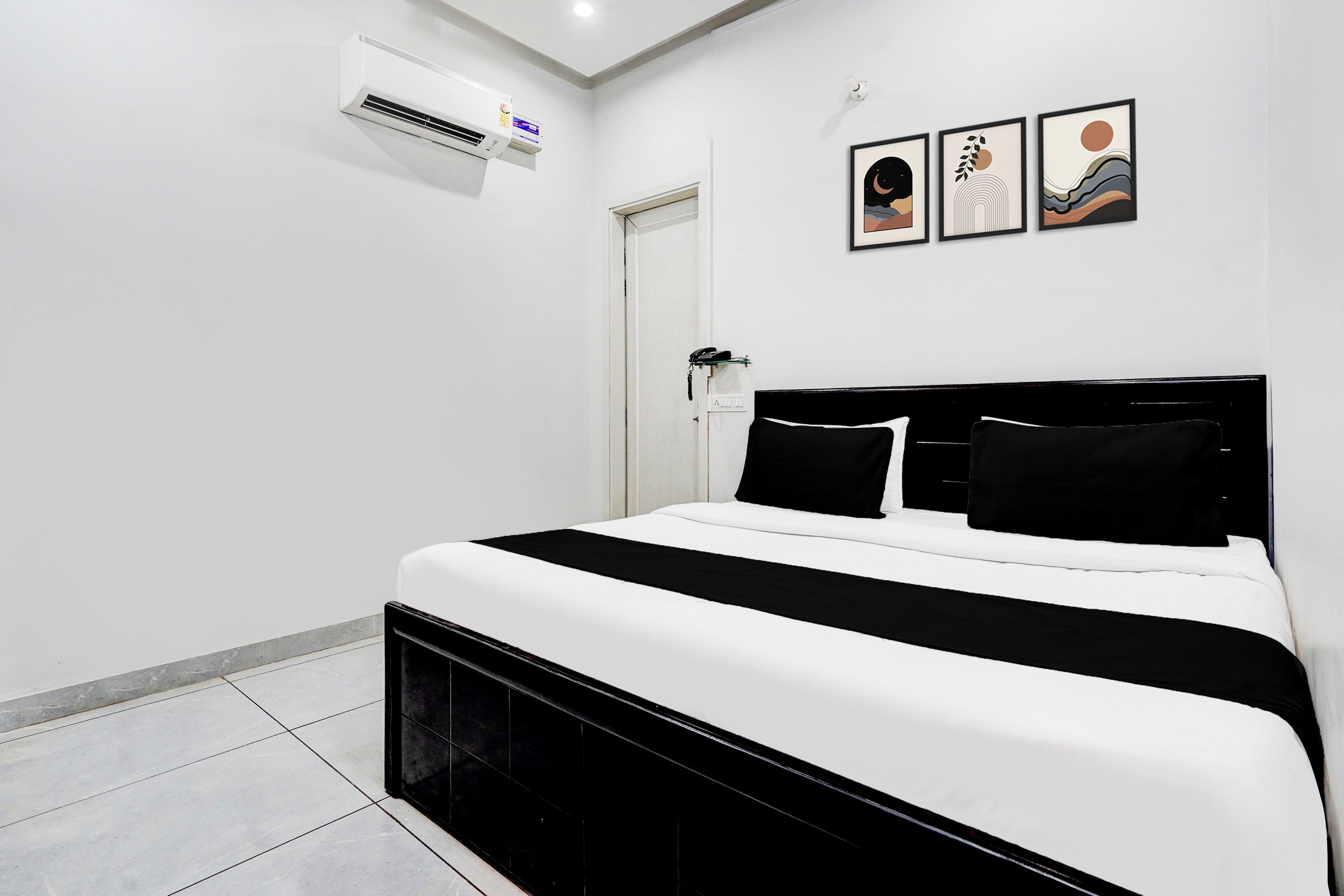 A hotel room with a bed, a wall-mounted air conditioner, and three framed artworks.