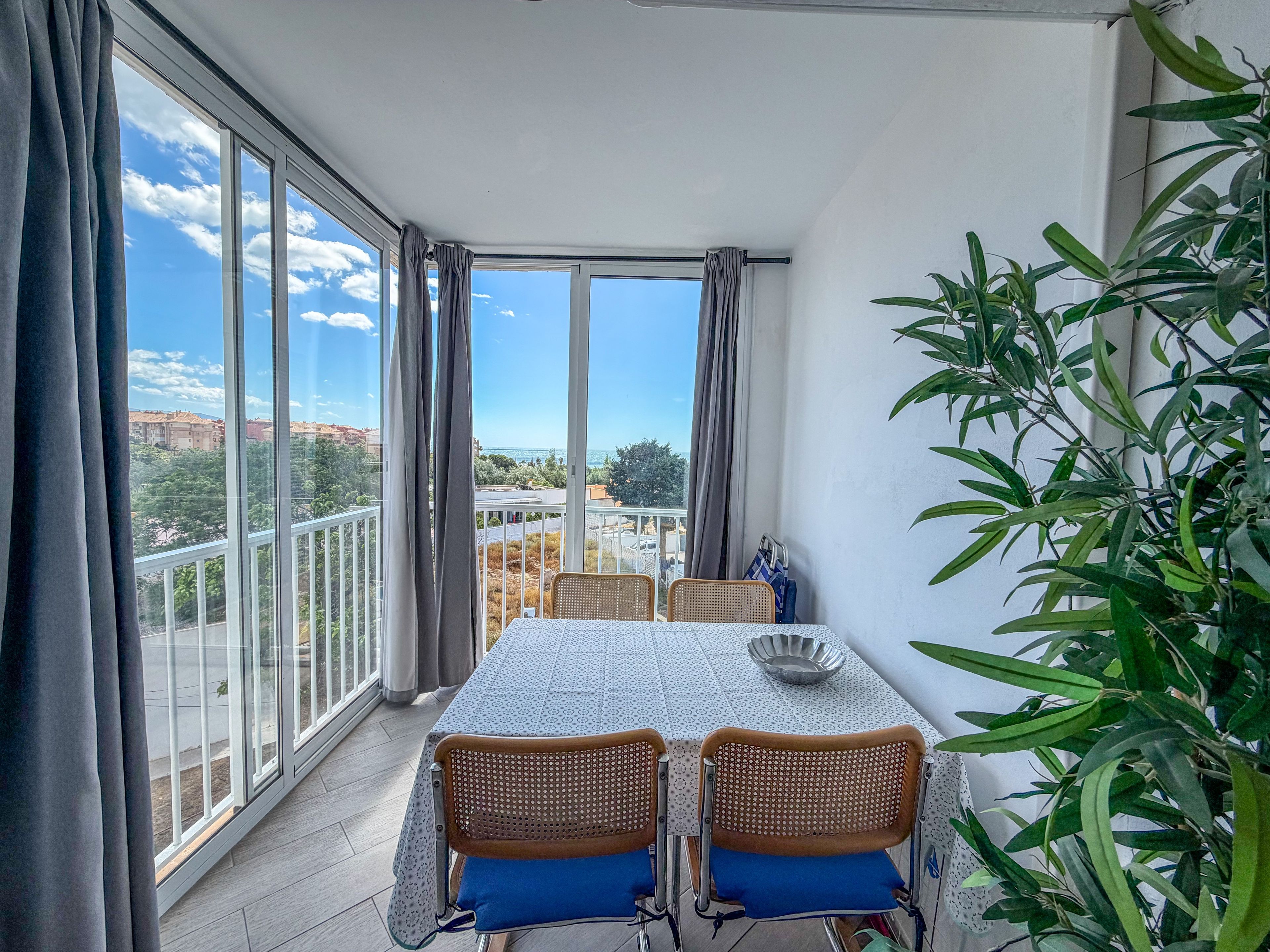 A balcony with a table and chairs, a view of the city, and a potted plant.