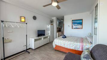 Una camera da letto con un letto, una scrivania, un armadio, una ventola a soffitto e vista sulla cucina.