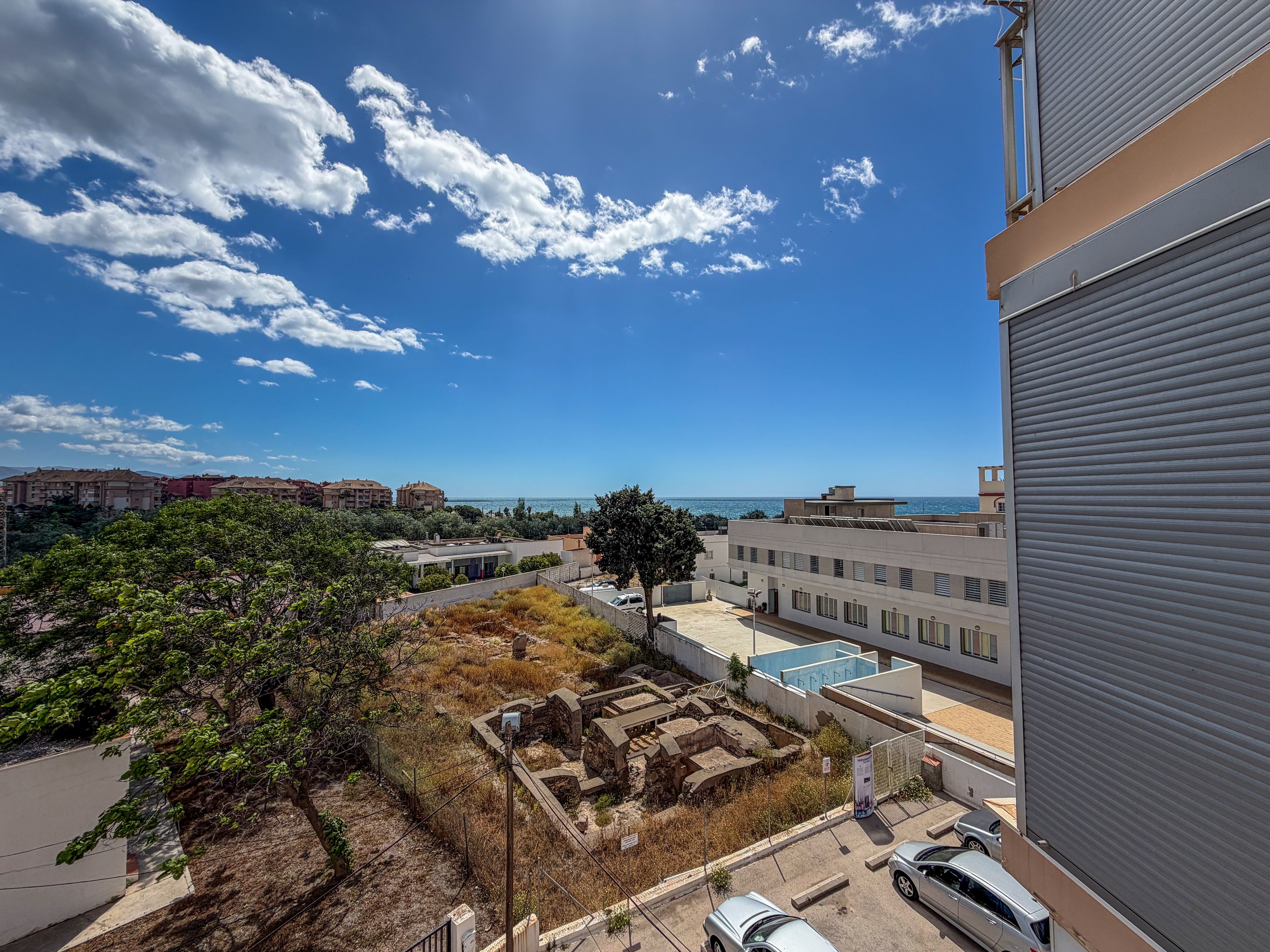 A residential area with a view of the sea, a tree, and a building with a closed shutter.