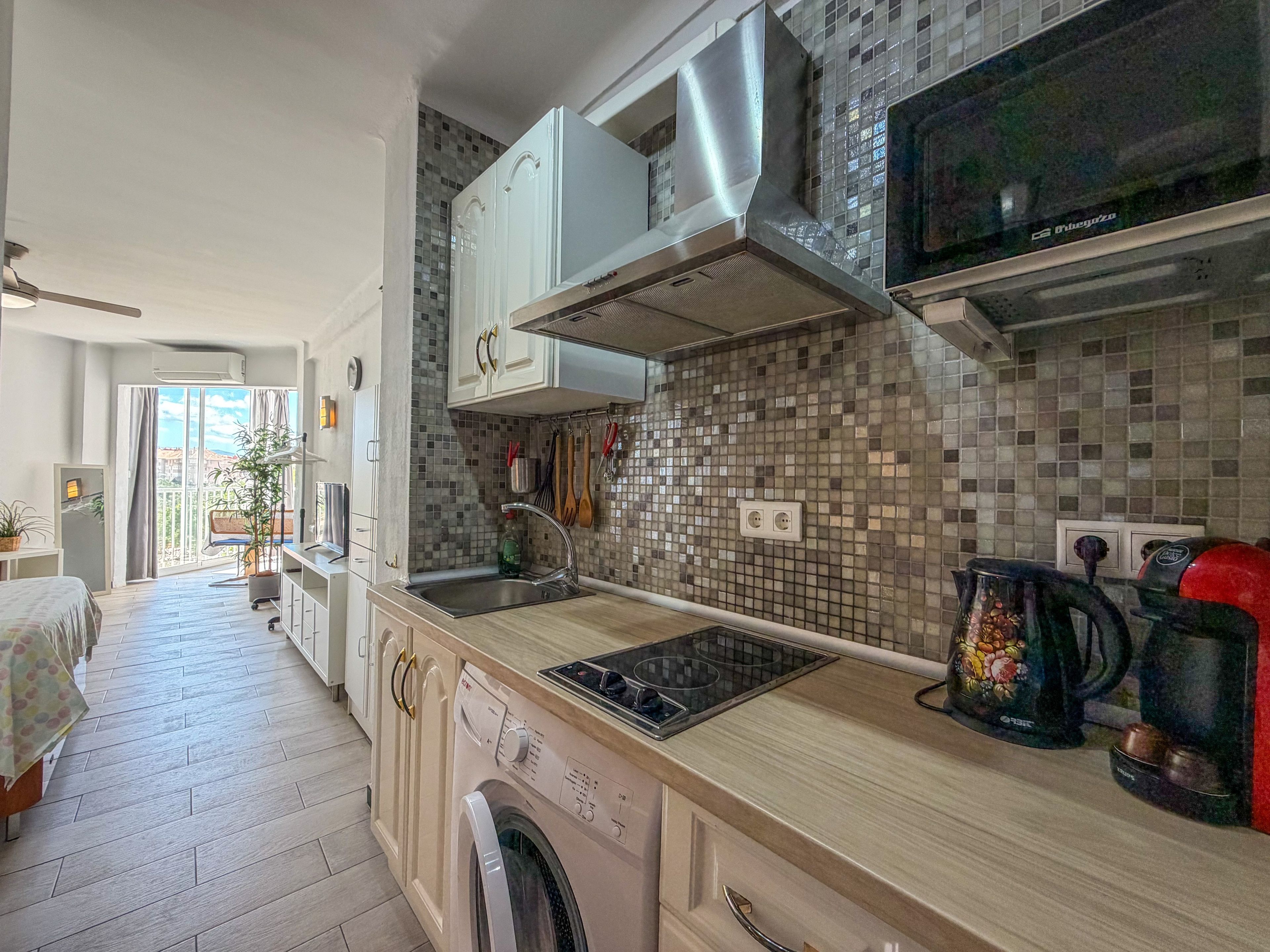A modern kitchen with a built-in washing machine, a microwave, and a coffee machine.