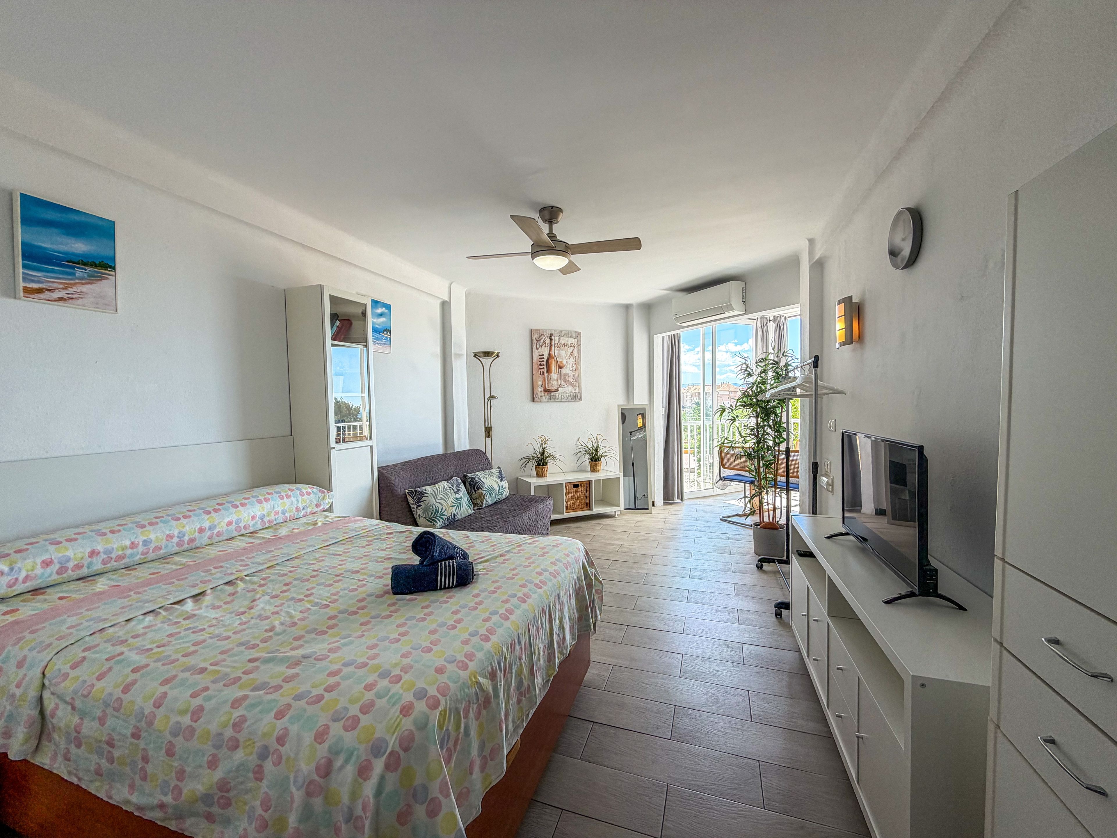 Een slaapkamer met twee bedden, een plafondventilator, een televisie en een groot raam.