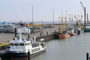 A harbor with multiple boats docked, a crane, and a building with a sign. - Holiday home in Hooksiel with swimming pool (Hooksiel)