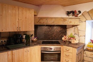 A kitchen with wooden cabinets, a stone backsplash, a built-in oven, and decorative items on the countertop. - Apartment 3 in the holiday home Traumweide (Oberwiesenthal)