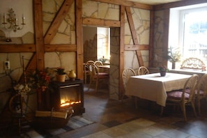 Een rustiek interieur met zichtbare houten balken, een stenen muur, een open haard en een eethoek met stoelen en een tafel.