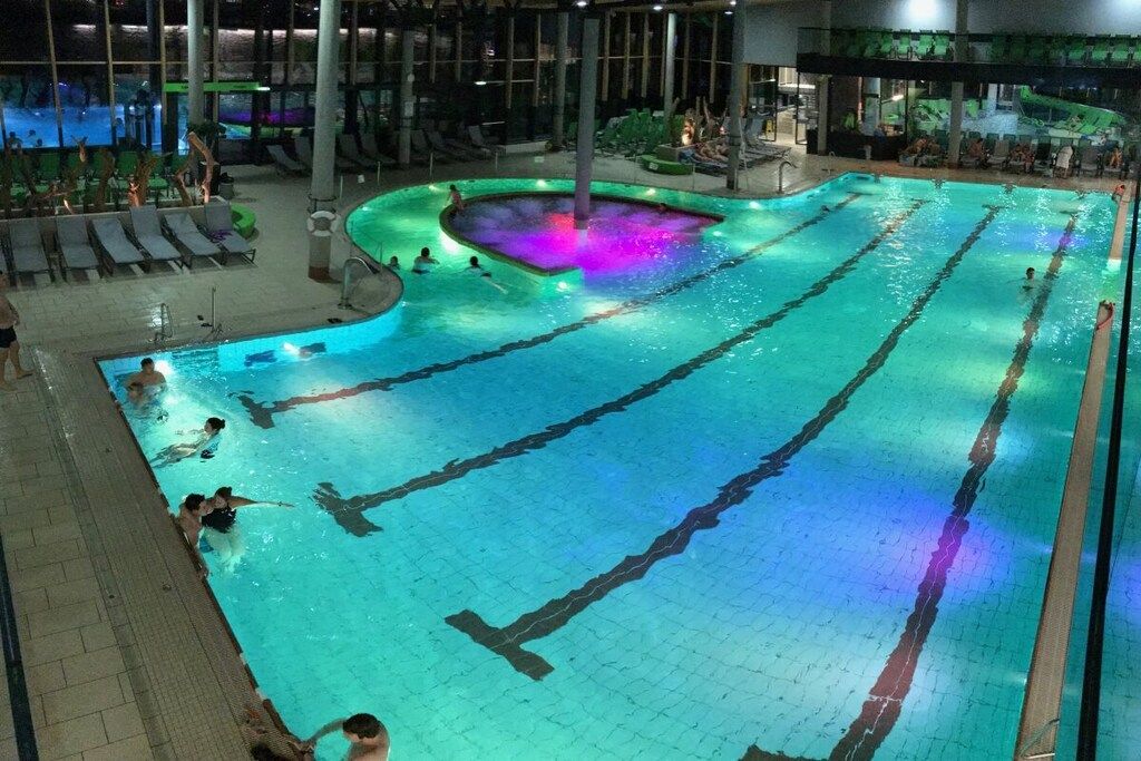 An indoor swimming pool with multiple lanes, lounge chairs, and a central hot tub area.