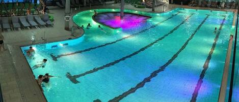 An indoor swimming pool with multiple lanes, lounge chairs, and a central hot tub area.