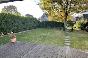 Eine Holzterrasse mit einem Blumentopf, einem Rasen und einem Heckenstreifen.