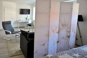A modern living room with a sofa, a chair, a coffee table, a TV mounted on the wall, and a lamp. - Apartment in Kiel-Mitte with swimming pool (Kiel-Mitte)