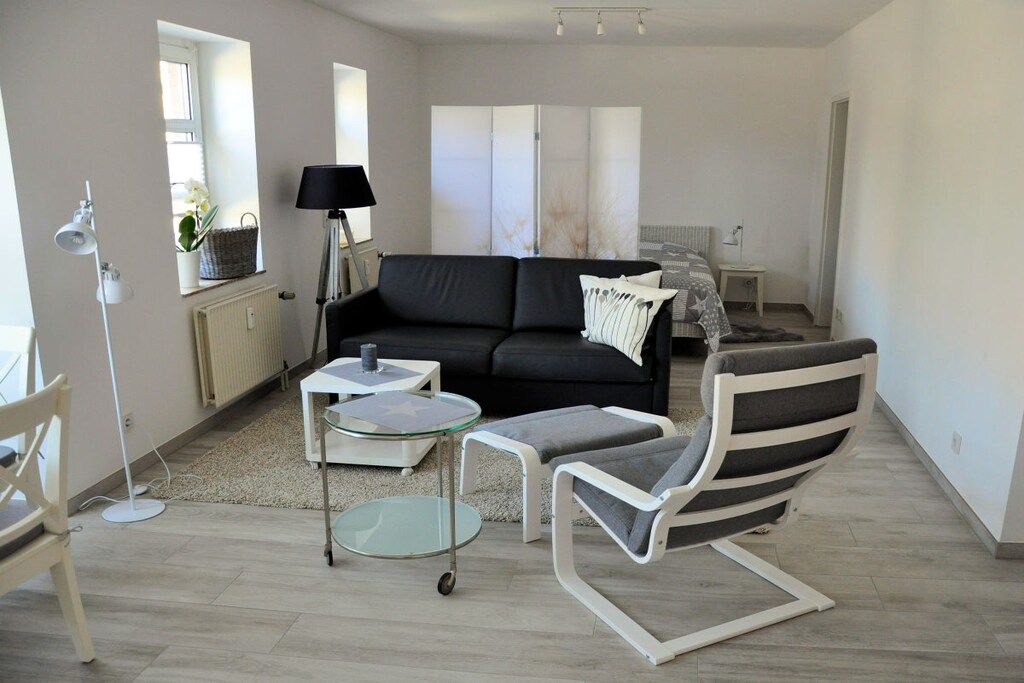 Ein modernes Wohnzimmer mit einem schwarzen Sofa, einem Glastisch, einem weißen Sessel und einer Stehlampe.