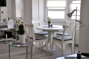 A modern office space with a round white table, four white chairs, a glass coffee table, and a potted plant. - Apartment in Kiel-Mitte with swimming pool (Kiel-Mitte)