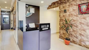 A hotel reception desk with a sign indicating it is a company-serviced hotel. There is a potted plant to the right of the desk.