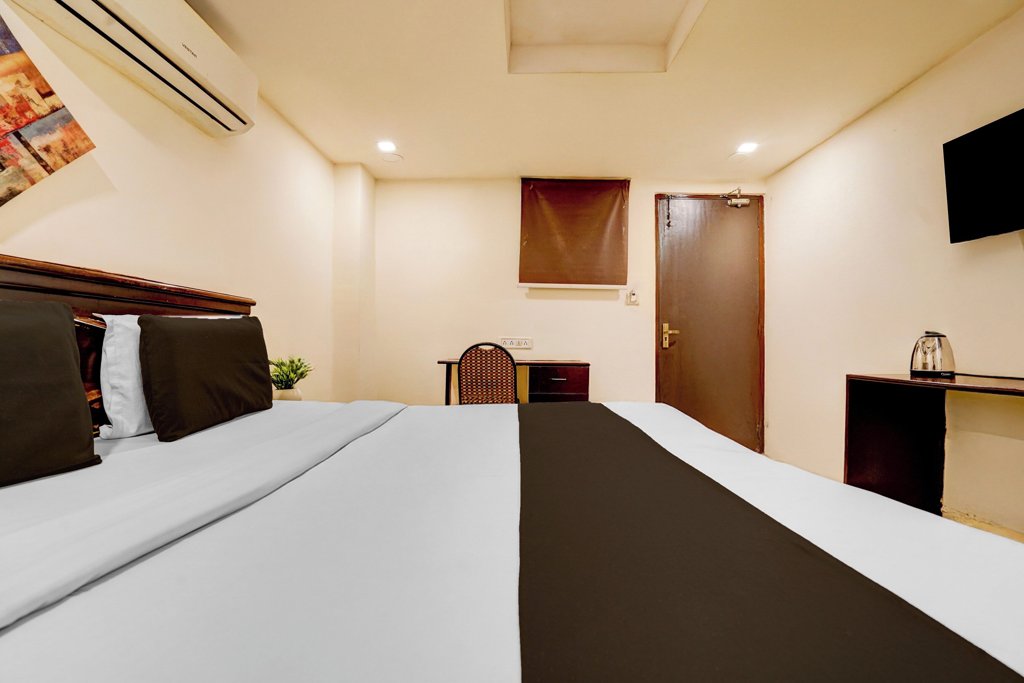 A hotel room with a bed, bedside table, chair, desk, and a television mounted on the wall.
