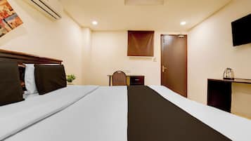 A hotel room with a bed, bedside table, chair, desk, and a television mounted on the wall.