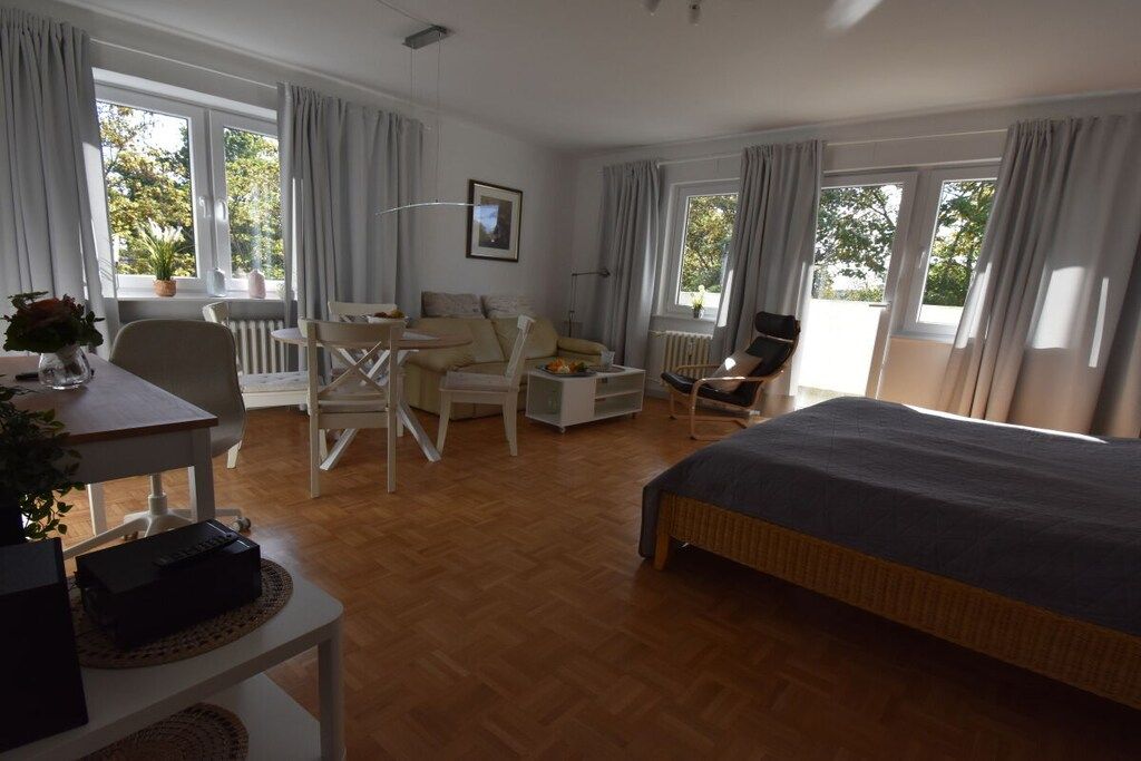 A hotel room with a bed, a desk, a chair, a small table, and a potted plant.