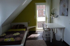 A small, well-lit room with a bed, a desk, and a window with a view of a brick building. - Holiday home with 2 bedrooms (Wangerland-Hooksiel)